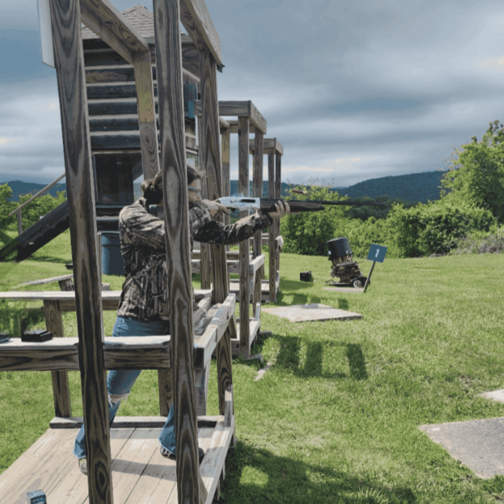 Kassi Redifer practicing clay target shooting at an outdoor shooting range with mountain views in the background.