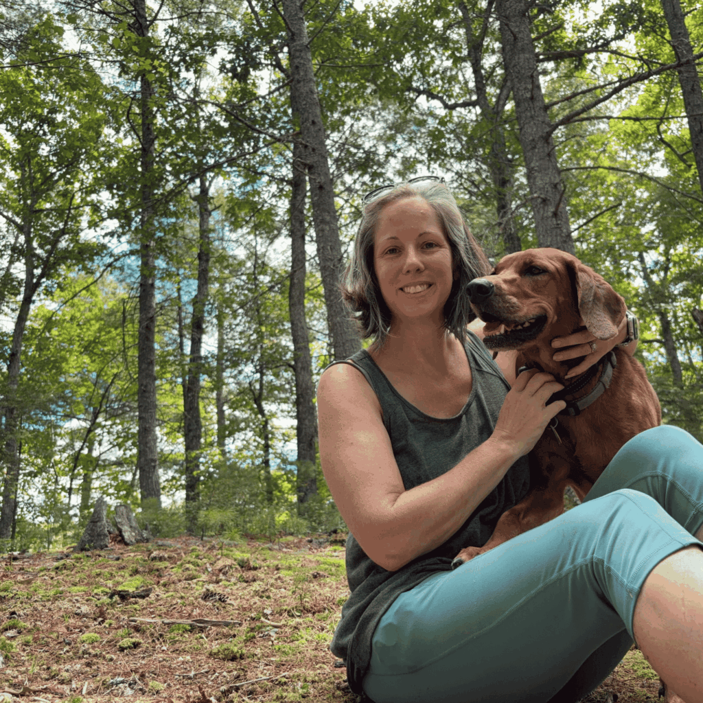 Marcy Holbert sitting with her dog Willow on a wooded mountain trail in Sugar Grove, West Virginia.