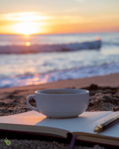 A cup of coffee resting on an open journal at sunrise by the ocean, symbolizing reflection, clarity, and intentional living during life’s transitions.